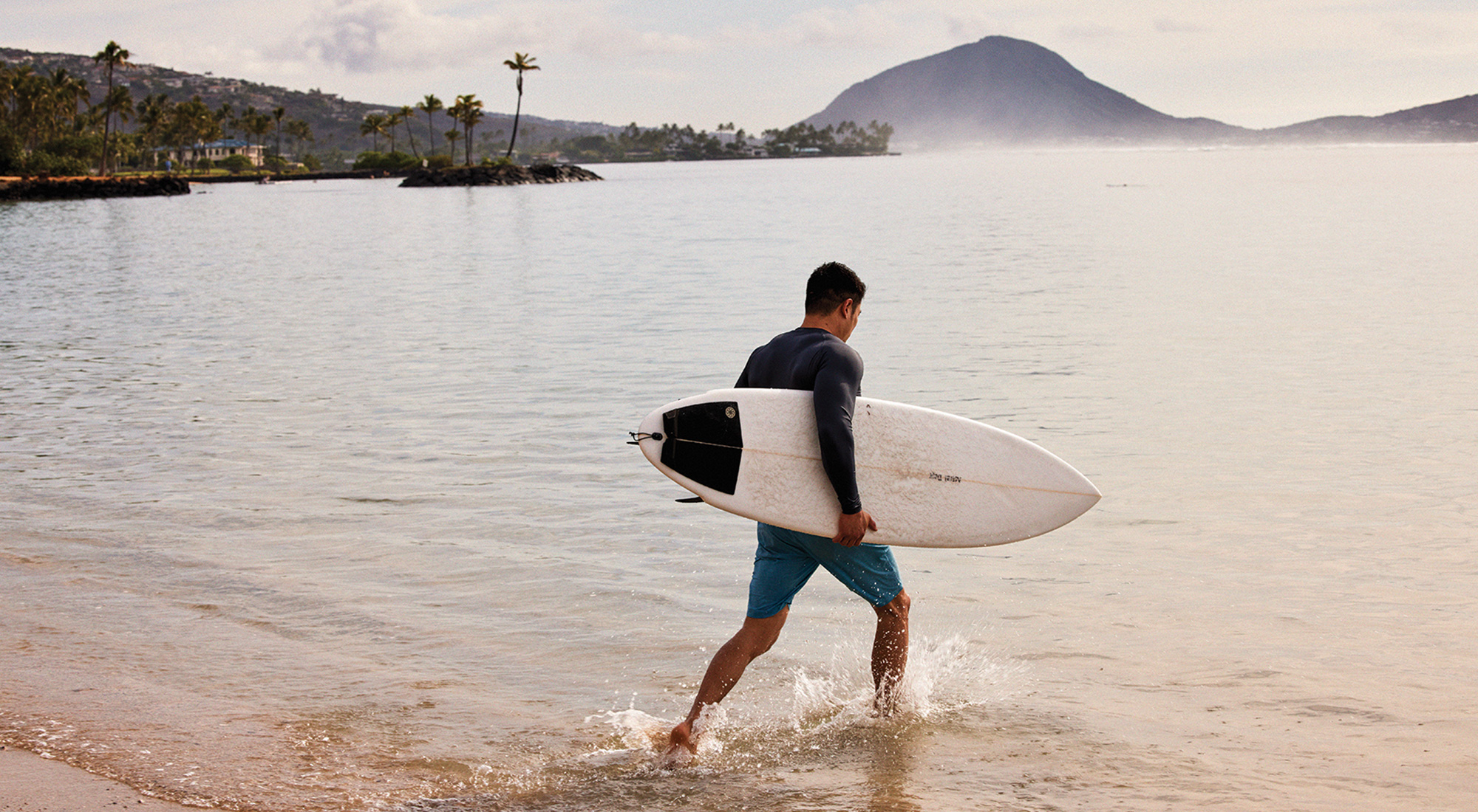 Surfer with surfboard walking into beach water